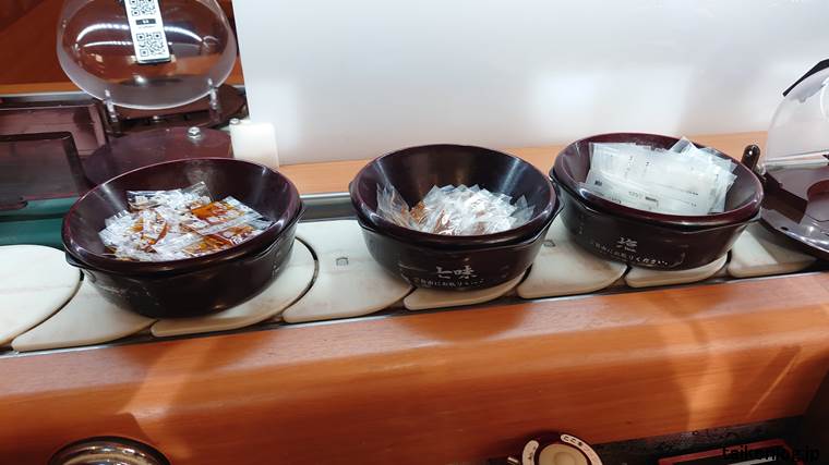 くら寿司の回転レーン上にある個包装された七味唐辛子、ぽん酢、塩